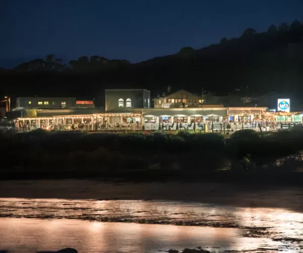 Sam's Chowder House lit up by lights at night as seen from across the water at the beach